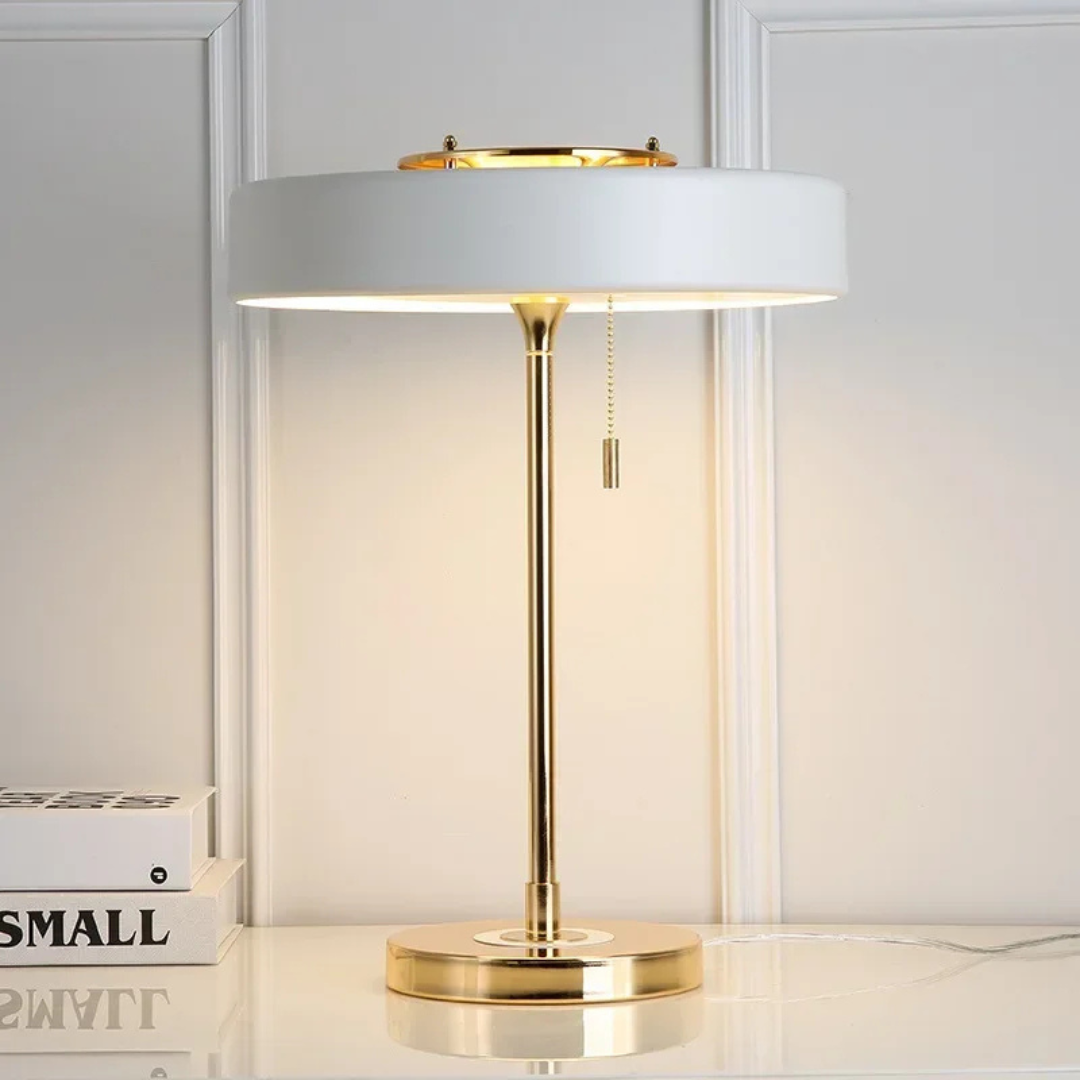 Table lamp with white shade and gold base on a light-colored surface.