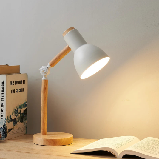 Table lamp with wooden base and white shade on a desk next to an open book.