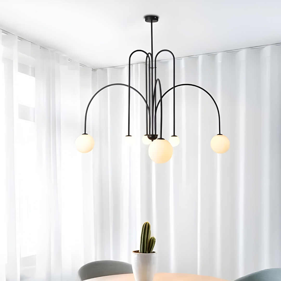 Modern chandelier with three hanging lights in a room with white curtains and a plant.