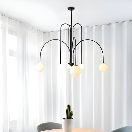 Modern chandelier with three hanging lights in a room with white curtains and a plant.