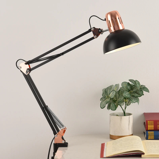 Black desk lamp with a copper accent on a surface with books and a plant.