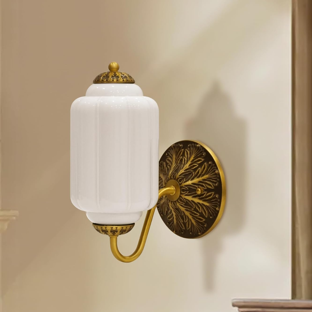 Decorative wall sconce with white glass shade and gold metal fixture on a beige wall.