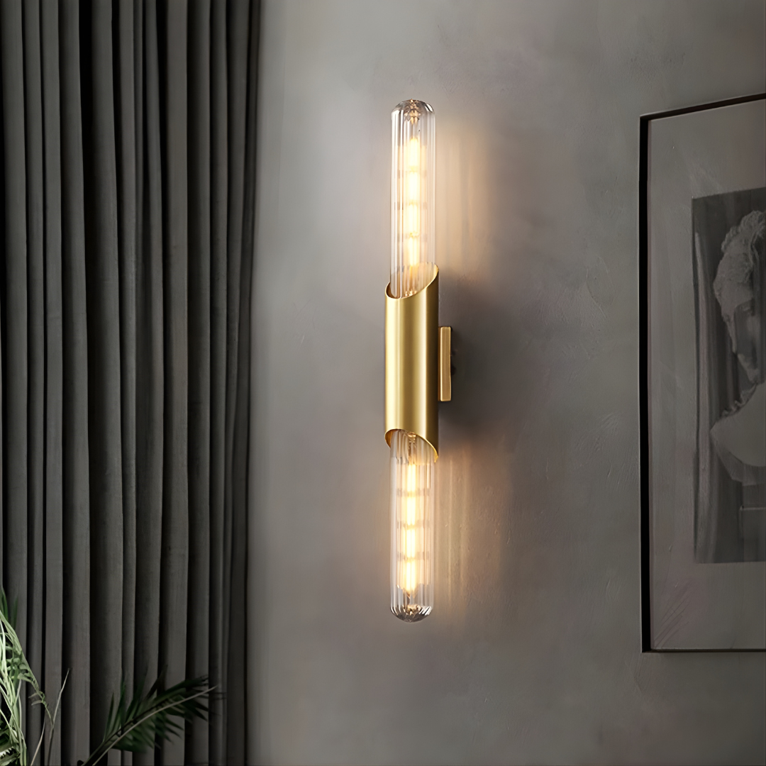 Gold wall sconce with clear glass shades on a gray wall.
