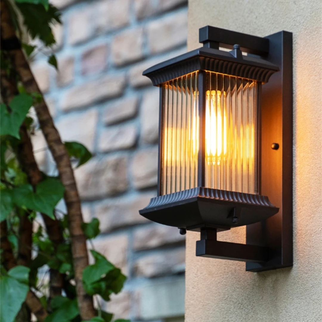Outdoor wall light fixture on a stone wall with a plant in the foreground